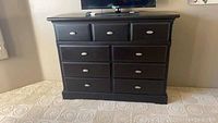 Front view of the black dresser with nine drawers and brushed nickel handles, showing overall structure and condition.