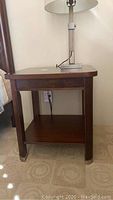 Wood end table with lamp on top, showing overall shape and design including detailed legs and metal feet.