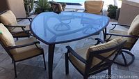 Overall view of triangular tempered glass table and six cushioned swivel chairs on stone patio