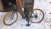 Blue Specialized Rockhopper mountain bike standing outside on snow near wooden structure with blue floor pump beside it.
