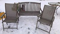 Wooden bench and two mesh folding chairs arranged outdoors on snow-covered ground