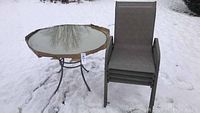 Round table with glass top on metal legs, in snow, with four stackable chairs beside it