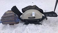 Wide view of the portable Weber grill with attached propane tank and bag of firewood on snow