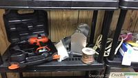 Black and Decker cordless drill with battery, carrying case, copper wire spool, metallic vents, and fasteners on a black plastic shelf.