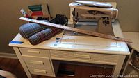 Wide shot of vintage Singer sewing machine with measuring stick and sewing forms on white sewing table with drawers