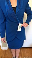 Front view of a woman modeling the blue blazer and skirt; blazer has embroidered and beaded satin lapel