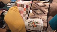 Overview of all three textile items: patchwork quilt, floral fabric wall hanging, and geometric patterned blanket folded on a couch.
