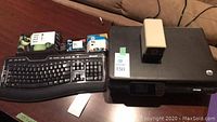 Photo of HP printer with Microsoft keyboard and HP ink cartridges on a table, with electric pencil sharpener on top of printer.