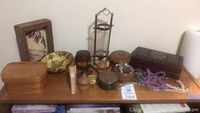 Photo showing assorted décor items on top of the wooden bookshelf including wooden boxes, decorative bowl, small containers, a framed wooden piece, some necklaces, and a tiered candle holder.