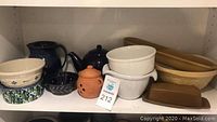 Shelved assorted pottery including bowls, teapot, garlic keeper, baking dishes.