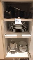 Black cups stacked on upper shelf, white plates and a creamer pitcher below