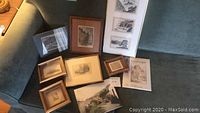 Collection of assorted small framed and unframed art prints, drawings, and photos arranged on a blue sofa.