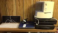 Wide view photo showing all items: humidifier, laptop, keyboard, DVD and VCR players stacked.