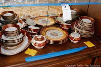 Full view of entire china dinnerware set arranged on wooden surface showing bowls, plates, cups, and platters with red and gold gilt design.