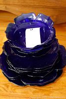Stack of cobalt blue flower-shaped dinnerware pieces including plates and bowls, showing deep blue color and flower petal edges.