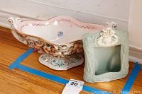 View of Capodimonte narrow bowl and light green picture frame together on floor with blue tape markings