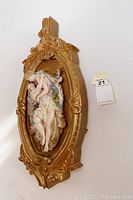 Side view of one gold gilt oval frame with 3D classical female figure plaque showing thickness and ornate edges.