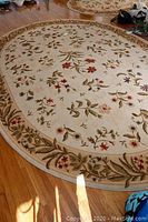 Full view of the oval rug showing its floral pattern and beige background on a hardwood floor.