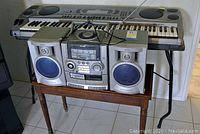 Casio electronic keyboard on black stand with Aiwa boombox on wooden bench below