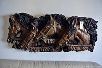 Front view of the horse wall relief sculpture showing three horse heads with dark textured finish hanging on a wall.