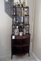 Full front view of the wooden corner curio shelf showing multiple shelves with decorative cut-out panels and mirrored back, placed at a room corner.