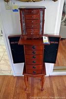 Front view of both wooden jewelry cases stacked: smaller tabletop box on top and floor chest below with side doors open showing black velvet interior.