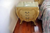 Front view of the vintage nightstand showing three drawers with ornate handles and custom cut glass top