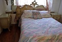Full view of king size carved headboard with optional queen mattress bed dressed with pastel patterned bedding and two matching nightstands.
