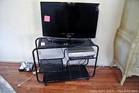 Samsung 32-inch TV, Sylvania VCR/DVD player on the black metal cart with three shelves, showing full setup and condition.