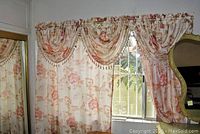 Curtain set hung on a window showing floral patterned panels with matching valance and beads.