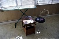 Wide shot showing all items: ironing board frame, vanity chair, side table.