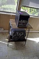 View of the vintage boom box placed on a wooden table with metal hairpin legs. The table top needs replacement glass.