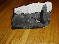 Two irregular shaped soapstone artworks depicting flying geese in a natural landscape with a sun, detailed with engraving and dark coloring.
