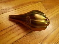 Iridescent seashell-shaped glass paperweight with Robert Held Art Glass sticker on wooden floor.