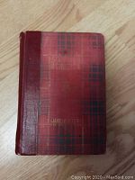Front cover view of the hardcover book showing the red plaid pattern with gold embossed title and author text. Shows wear and condition of the book cover.