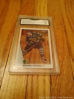 Front view of Mitchell Marner 2015 Leaf Acetate rookie card graded Gem Mint 10 in protective slab on wooden floor.