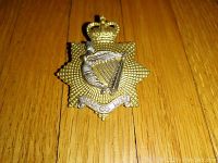 Front view of Canadian Irish Regiment cap badge showing crown, harp, and motto on metal star background.