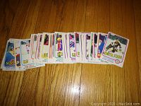 Photo showing a spread of about 30 hockey cards from the lot, face up in a fan arrangement on wood floor, featuring various players with white border design and colorful team names along bottom edge.