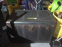 Front view of dark covered steamer trunk with brass hardware and lock plate, showing size and wear.