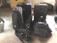 Photo showing most of the 10 pieces including two black rolling expanding suitcases, padded camera bag, and several carry bags grouped on the floor.