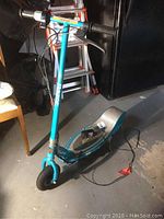 Full view of blue electric Razor scooter on concrete floor with attached charging cable.