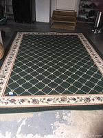 Full view of green nylon fiber area rug with floral border and lattice flower pattern, showing size and condition.