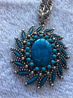 Close-up of the front of the pendant showing central oval blue stone circled by small round blue beads and silver-tone metal decorations