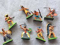 Overhead view of all 8 vintage Britain's Native American warrior figures arranged on light background, showing variety of poses and colors