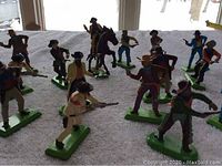 Group of plastic Cowboys and Gunfighters figurines arranged on a white towel, some standing and one mounted on a horse, showing variety and color detail.
