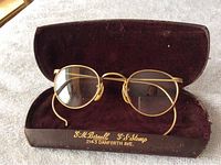 Front view of the round gold filled antique reading glasses placed inside the brown velvet-lined case with gold embossed text.