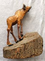 Photo of side view of wooden baby moose carving on wood base showing body and bark details.