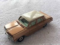 Photo showing the front and side angle of the toy car on a soft white surface, capturing the white roof and light brown body details.