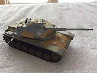 Front and side view of old die cast metal military tank toy, showing camouflage paint, star insignia and address numbers on front plate
