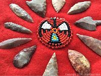 Twelve flaked stone arrowheads arranged in a circular pattern around a beaded center on red felt.